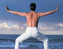 Person demonstrating a postural balance pose on a beach with arms extended